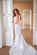 Vestido de noiva sereia com detalhes em renda, apresentando uma modelagem que abraça as curvas com elegância e termina com uma cauda longa e fluida. A peça exibe sofisticação e um design atemporal, perfeito para noivas brasileiras modernas e clássicas. A modelo, posicionada em um ambiente com decoração vintage, evoca uma atmosfera romântica, ideal para quem busca inspiração para casamento com um toque de estilo e personalidade.