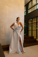 O vestido de noiva "Pilar" da coleção Barcelona da Luuly Noivas apresenta um design elegante e moderno. Feito em tecido Zibeline branco, possui uma silhueta longa e fluida, com uma fenda frontal que adiciona um toque contemporâneo. O decote é em formato coração e a peça destaca-se por uma única alça larga no ombro esquerdo, terminando em um laço estruturado. O vestido é leve, confortável e ideal para diversas cerimônias, proporcionando à noiva um visual sofisticado e único.